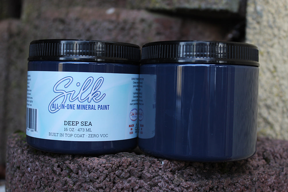 Peinture Silk de Dixie Belle. Couleur "Deep sea" bleur-noir. Peignez les profondeurs rafraîchissantes et mystérieuses de l'eau avec les teintes bleu-noir luxuriantes de Deep Sea. La peinture Silk All-In-One est une peinture crémeuse et auto nivelante en une seule étape. Il a un bloqueur de taches intégré (à base d'eau), un apprêt et une couche de finition. Résistante à la moisissure. Vous pouvez utiliser cette peinture à l'intérieur car elle est inodore et non toxique.